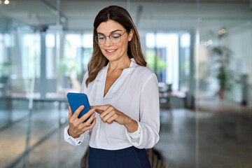 Happy mature female employee or professional bank manager looking at cell mobile phone tech at...