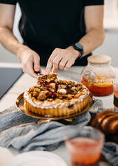 A person serving a piece of a delicious fruit tart, garnished with nuts and powdered sugar