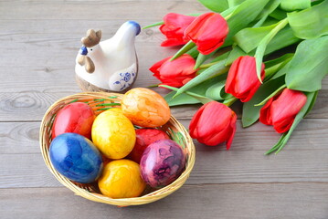 Easter eggs in basket, red tulips and ceramic hun on wooden background.