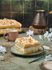 Norwegian dessert, sliced best cake with meringue, almonds and custard on a dessert plate on a green concrete background. Norwegian cuisine.