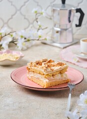 Norwegian dessert, sliced best cake with meringue, almonds and custard on a pink dessert plate on a light concrete background. Norwegian cuisine.