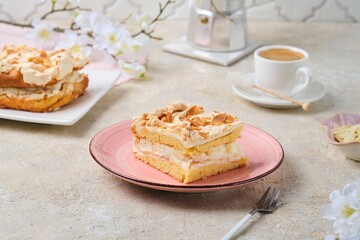 Norwegian dessert, sliced best cake with meringue, almonds and custard on a pink dessert plate on a light concrete background. Norwegian cuisine.