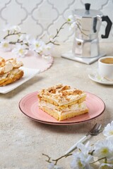 Norwegian dessert, sliced best cake with meringue, almonds and custard on a pink dessert plate on a light concrete background. Norwegian cuisine.