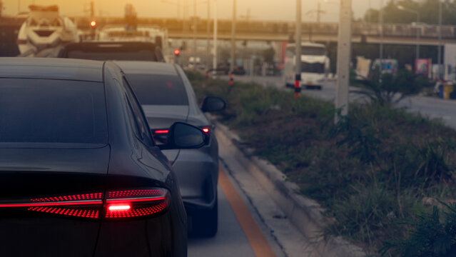 Rear side of dark car turn on brake light. Traffic cars on the asphalt road. With green island in center road. blurred of bridge across the front. Environment of evining time.