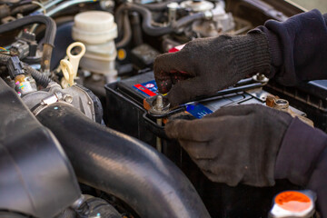 Replacing a car battery. The mechanic installs the battery, securing the battery mounting bracket...
