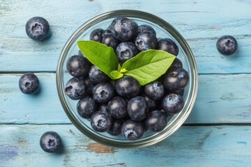 Fresh blueberries in a glass bowl with mint leaves resting on a rustic blue wooden table