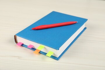 Book with colorful tabs and pen on light wooden table, closeup