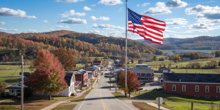 Small American town with a prominent United States flag flying against a bright autumn landscape, showcasing colorful foliage, rolling hills, and a clear blue sky - Powered by Adobe