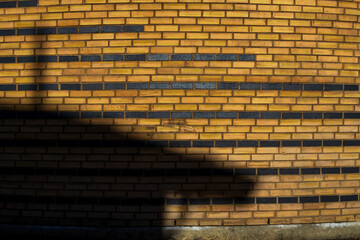 A yellow brick wall with multiple black brick lines is transformed by a shadow, creating an...