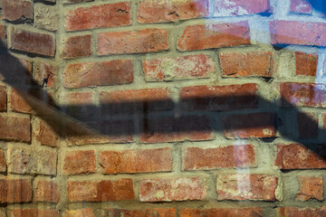 A red brick wall seen through a window is marked by a sharp, angular shadow stretching across in a...