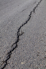 A diagonal crack stretches across the asphalt road, revealing the textured surface and subtle imperfections of weathered pavement.