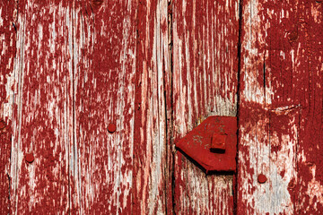 An old red-painted metal triangle with a square nail sits against weathered wooden planks, where...