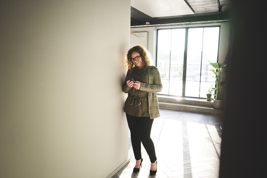 Smiling businesswoman standing in a hallway reading a text message
