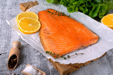 Hot smoked trout fillet, lemon slices and thyme on white paper, salt and pepper on grey background