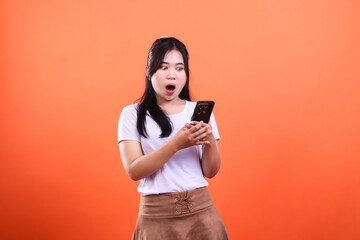 Naklejka premium Woman holding black smartphone with an amazed face in front of orange background