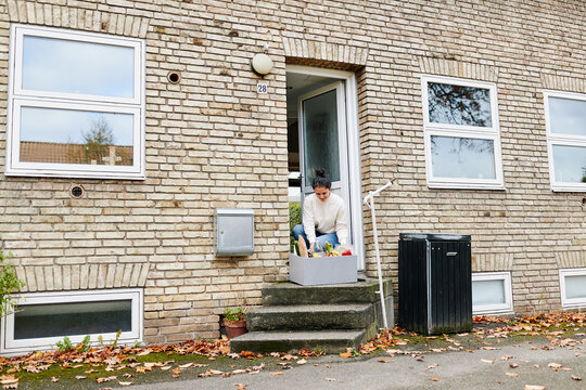 Woman picking up grocery delivery at her door. She gets fresh products delivered, thus avoiding having to shop in a store.