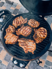 Juicy pork chops being grilled on a barbecue grill with savory seasoning, featured on an outdoor tiled patio. Perfect imagery for a cookout, outdoor meal scenes, or grilled food advertisement.