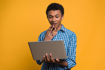 Surprised Afro American teen looks at laptop screen.
