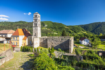 Jajce town in Bosnia and Herzegovina, Europe. Church of St. Mary with the tower of St. Luke. Historic stone tower and walls stand tall against a backdrop of lush green hills under a bright blue sky.