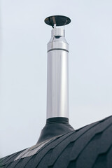 Galvanized metal chimney exhaust on asphalt roof with a rain cap