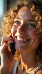 Close-up of a young woman with curly golden hair, laughing softly while talking on her smartphone