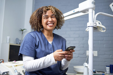 Smiling Dental Professional Holding Smartphone in Modern Clinic Office Environment