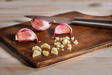 Garlic cloves next to chopped garlic pieces on a cutting board with a knife, close-up.