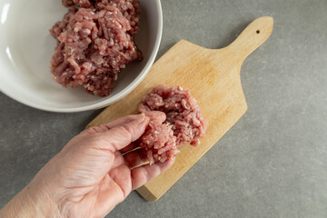 Raw ground meat on a wooden cutting board, in a bowl, and in a hand.