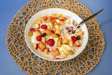 Oatmeal porridge with strawberry, apple, almond and nut, honey and butter in plate on circle bamboo pad on blue.