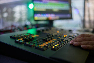 Closeup image of a hand mixing sounds on a control board, showcasing an audio technicians work