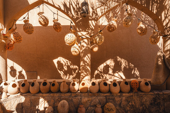 handgefertigte Tongef&auml;&szlig;e an Lehmmauer in arabischem Stil in Szene von den Schatten eines Palmenblattes in Beige- und Braunt&ouml;nen