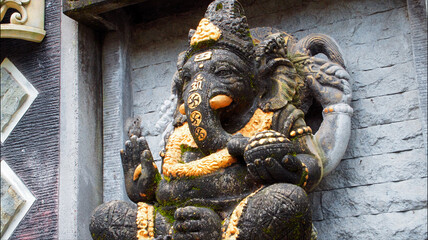 An old hindu stone statue of Ganesha covered with moss, standing on the str..