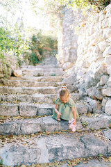 Little girl squats on old stone steps in the garden playing with a toy mouse