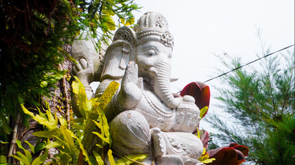 An old hindu stone statue of Ganesha covered with moss, standing on the str..