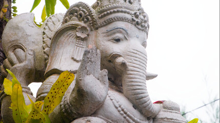 An old hindu stone statue of Ganesha covered with moss, standing on the str..