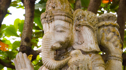 An old hindu stone statue of Ganesha covered with moss, standing on the str..