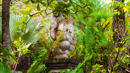 An old hindu stone statue of Ganesha covered with moss, standing on the str..