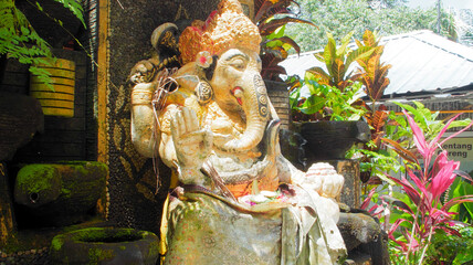 An old hindu stone statue of Ganesha covered with moss, standing on the str..