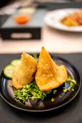 Two delicious samosas resting on a bed of lettuce on a black plate