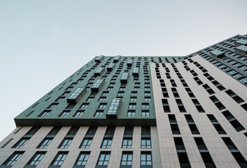 Stylish high-rise residential building at dusk against light blue sky. Looking up at the facade of modern building with multi-colored facade. 