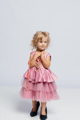 Little girl in a pink dress with pearls posing gracefully against a neutral background