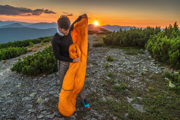 A traveler in the mountains spreads out an orange sleeping bag in the wind during an Alpenglow...