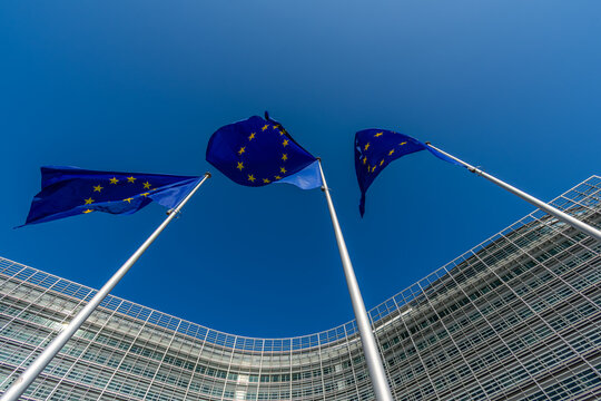 Bruxelles, Belgique - 8 mars 2025: Trois drapeaux europ&eacute;ens, symboles de l'Union Europ&eacute;enne, flottant contre un arri&egrave;re-plan de ciel bleu avec le b&acirc;timent Berlaymont, si&egrave;ge de la Commission Europ&eacute;enne
