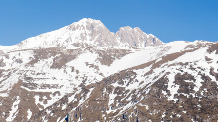 Obraz premium Aerial view of the peak of a winter mountain on a sunny day. There is white snow between the rocks.