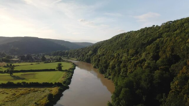 Aerial drone footage crossing the River Wye with Tintern Abbey in the background on a sunny summer day, capturing scenic landscapes and historic architecture.