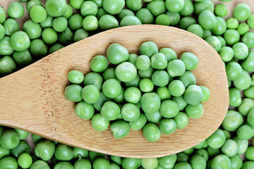 Fresh and young green peas in wooden spoon, top view