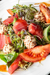 A colorful garden salad featuring fresh tomatoes, vibrant greens, and savory cheese balls, garnished with microgreens for an appealing presentation.