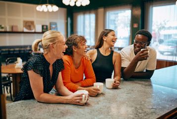 Group of diverse friends laughing and enjoying coffee at a cozy cafe, while they are on break from their work.