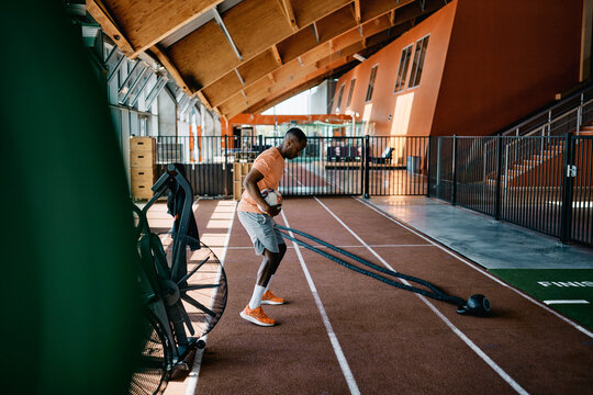 Fit young black man in sports clothing focused on doing a workout with a foam roller alone on a the floor of a gym