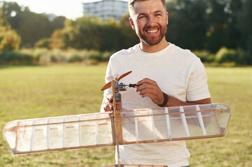 Made of wood. Man is on the field fixing the toy plane